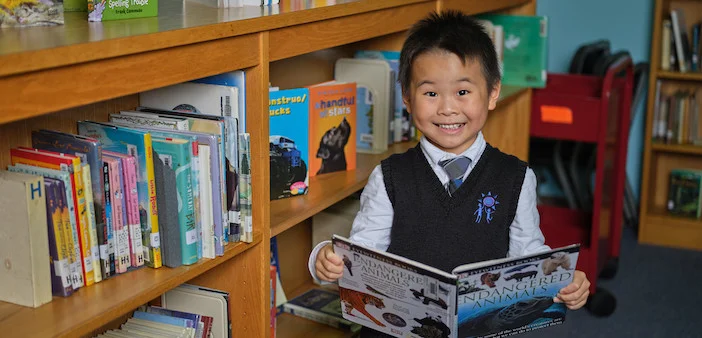 An image of a smiling child holding a book in their school library