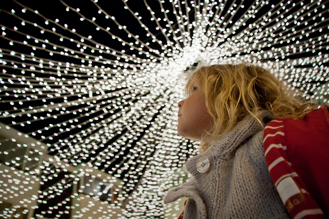 A girl looks upwards at Christmas lights