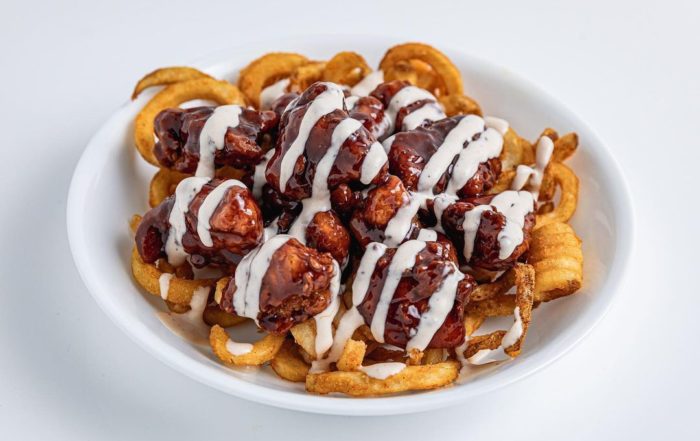 A bowl of curly fries topped with chicken nuggets spun in sauce and drizzled with ranch from Bad Chicken.