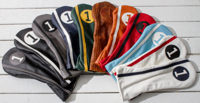 An array of Stitch Golf's headcovers for golf clubs. They are many colors, but each has a stripe down the side.