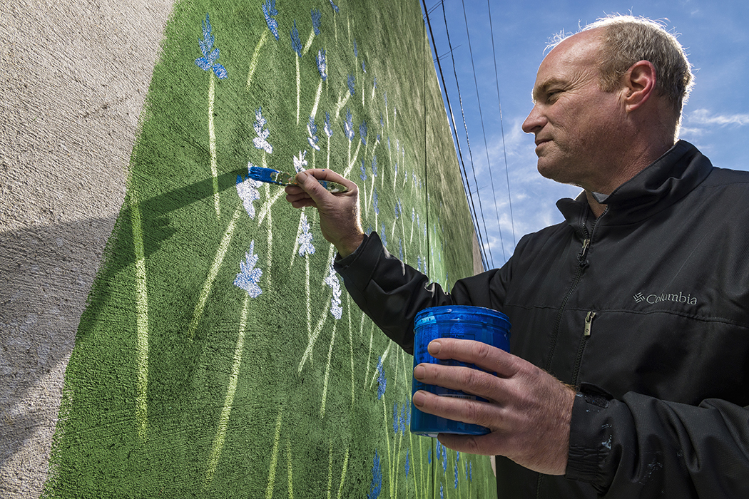 Brent Herling paints bluebonnets on the Marsh Lane mural. (Photo by Danny Fulgencio)